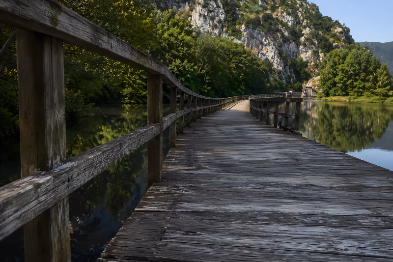 Cyclist crossing the wooden walkway over the Valdemurio reservoir, on the Quirós branch of the Ruta del Oso