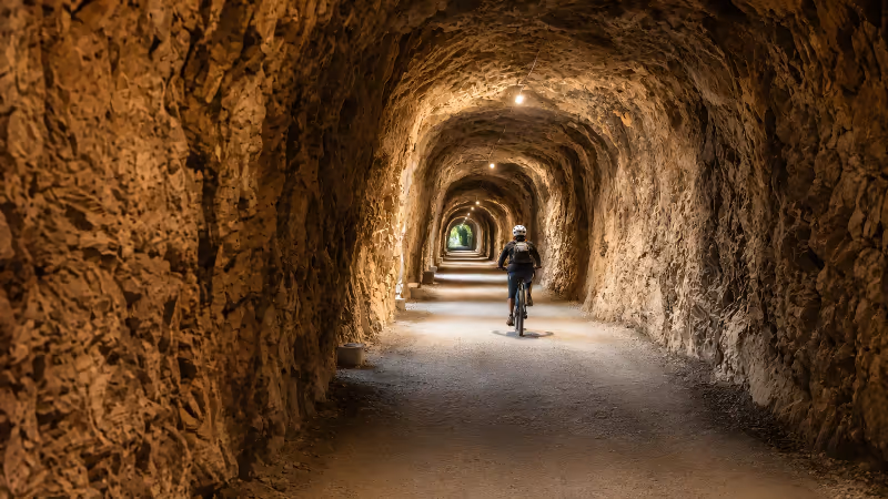 The Ruta del Oso trail passing under a double tunnel carved into the rock, with a wooden railing